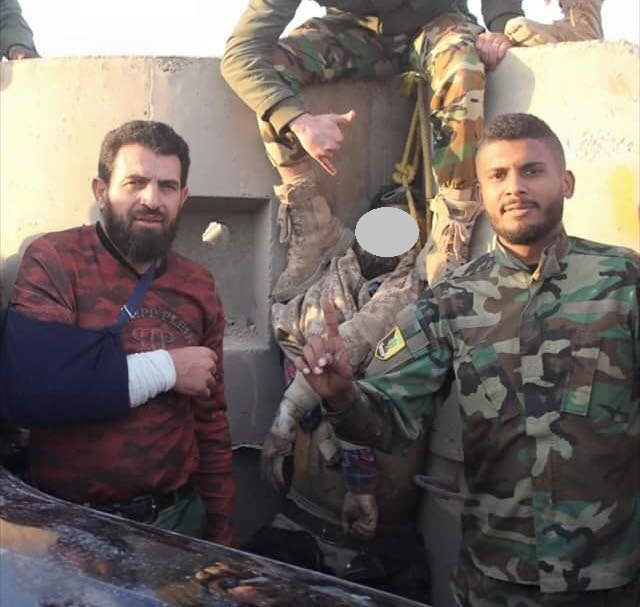 Wanis Bu Khamada’s son (R) posing with Jalal al-Makhzoum’s hanged corpse outside Al-Saiqa camp